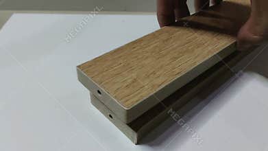 man\'s hand places three minimalist wooden boards stacked one by one on a white board.