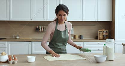Positive beautiful housewife woman in cooking apron rolling dough