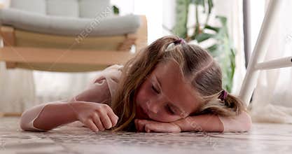 Child little girl is bored lying on the floor moving her hand along home floor