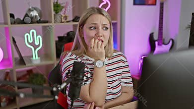 Stressed young blonde woman streamer biting nails, consumed by anxiety while at computer in gaming room