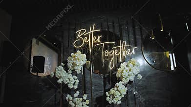 Neon glowing wedding lettering better together hanging on the wall over the beautiful floristic composition with white