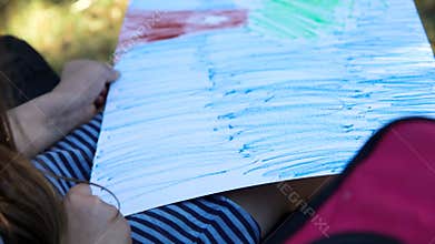 Girl draws a blue sky with a crayon on a large sheet of paper