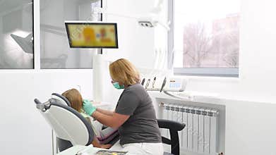 Pediatric female dentist treating little girl's teeth in the modern dental office. Doctor removes caries in little