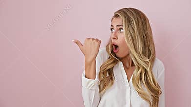 Astonished young blonde female in shirt joyfully pointing sideways, basking in amazing discovery! the pink backdrop sets her off
