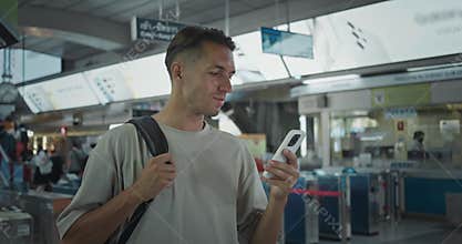 Mid adult Caucasian man stands in airport using smartphone. Departure boards shuffle of passengers millennial person