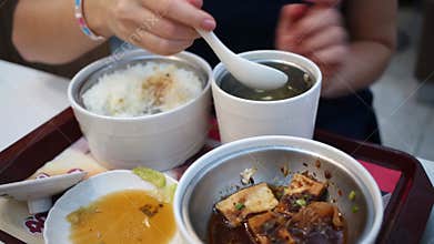 Hands of woman eating soup, rise, meat in pots in