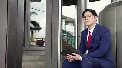 Professional young asian businessman in suit using tablet while sitting in modern office.