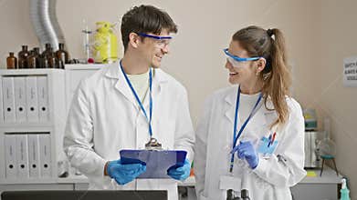 Two scientists, a man and a woman, collaborate in a lab, reviewing data together with a clipboard