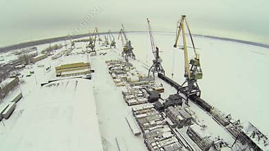 Hangars near tall cranes in cargo dock on shore of