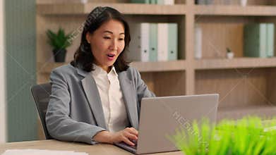 Middle-aged emotional amazed Asian business woman looking laptop feeling amaze surprised Chinese Korean businesswoman