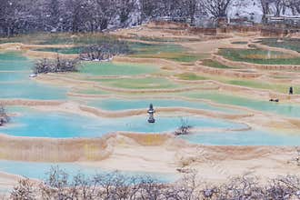 Turquoise travertine terraces with steaming pools and sparse winter shrubs creating serene natural landscape at Huanglong National