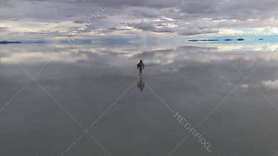 A solitary figure traverses the expansive Uyuni Salt Flats in Bolivia, captured in a serene early morning setting