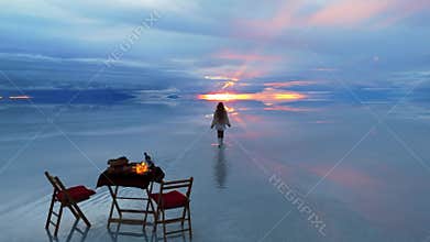 A woman walks across the serene Uyuni Salt Flats in Bolivia, capturing the breathtaking reflection of the sunset