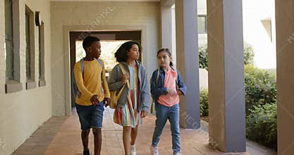 Three preteen students walking down school corridor with backpacks, chatting while heading to class