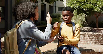 African American teens in courtyard with backpacks, girl initiating hand game, boy replying for fun