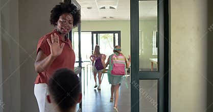 African American teacher welcoming children at door guiding backpacks into classroom, copy space