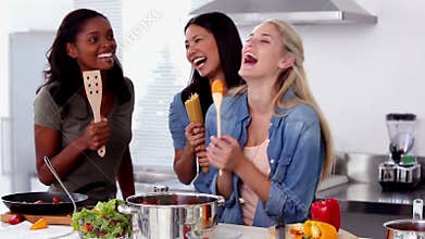 Laughing friends singing into a wooden spoon while cooking