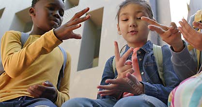 African youth friends playing finger game on steps with backpacks, denim jacket, passing time
