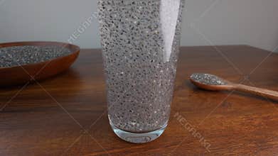 Glass filled with hydrated chia seeds creating gel-like texture with wooden kitchen utensils