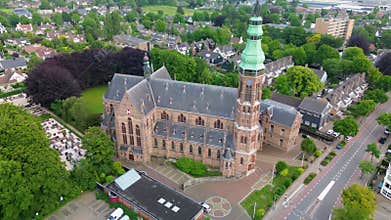 Aerial view of a grand historic church or cathedral with a tall green patina tower, arched windows, and stone detailing