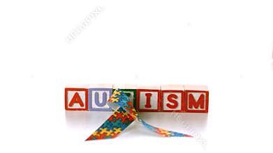 Awareness ribbon falling onto blocks spelling autism on white background