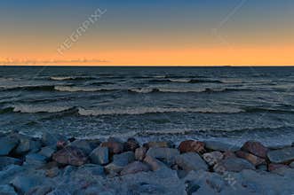 Beautiful sunset over the ocean with gentle waves breaking on a rocky shore in the evening light