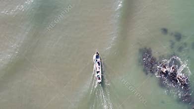 Top-down aerial view of a traditional fishing boat with fishermen navigating past a rocky reef in the ocean