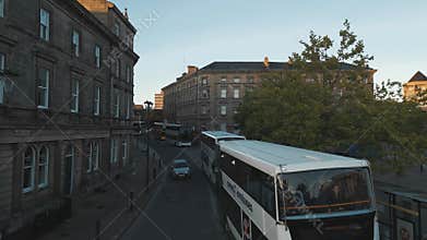 double-decker buses on street with historical stone buildings and pedestrians nearby in the morning