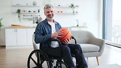 Man practicing basketball while seated in wheelchair in modern home environment
