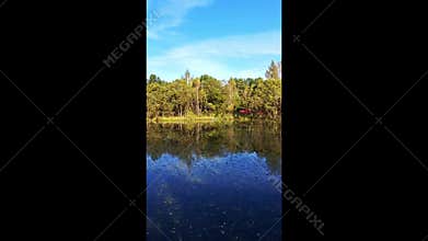Reflection of an autumn forest in the calm water of a lake against a blue sky
