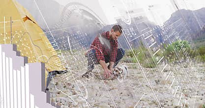 Male camper unwinding rope and driving stake after pitching tent to secure camping as petting dog