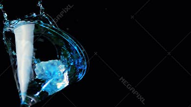 Ice falling into cocktail glass of blue liquid