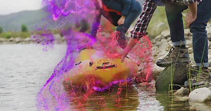Man and woman crouching on rocky lake shore guiding yellow kayak into water for outdoor adventure