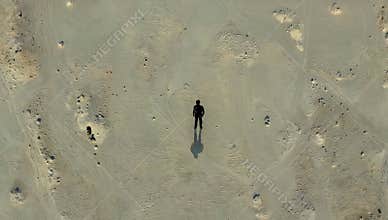 Aerial view of a lone figure standing in a vast desert landscape casting a shadow on the arid ground under the bright sunlight
