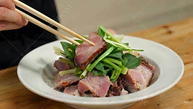 Delicious char siu dish with fresh green vegetables being picked up with chopsticks on a wooden table background setting