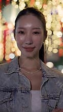 Portrait of pretty Asian woman in jacket smiles on illuminated evening street