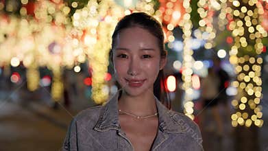 Portrait of pretty positive Asian woman with ponytail smiles on night street