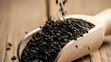 Black Cumin Seed Rain Falling into Wooden Spoon on a Rustic Wood Tabletop Close Up Nutritional Culinary Still Life Against Soft