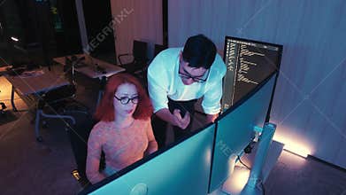 Two programmers in a modern office celebrate a coding breakthrough with a high five beside dual monitors displaying code, working