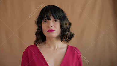 Close-up portrait of a woman with a dark bob haircut and straight bangs, looking directly at the camera, wearing a dark red top