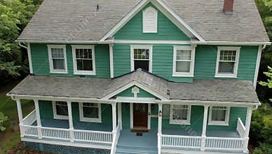 Charming green house with a welcoming porch and gray roof surrounded by lush green trees