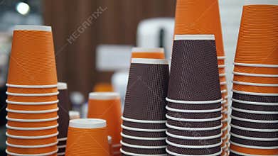 A vibrant stack of brown and orange paper coffee cups creates a visually appealing pattern in a shopping mall setting