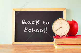 Blackboard with the phrase back to school, apple clock and stack of books. filtered image