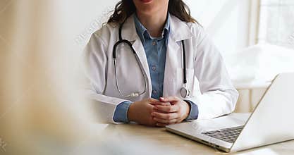 Doctor in coat sits at desk speaking with patient, closeup