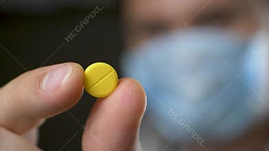 Healthcare expert in mask holding yellow pill as symbol of reliable treatment