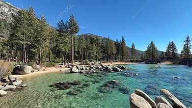 Wide scenic view of Sand Harbor beach cove with emerald water and pine forest background