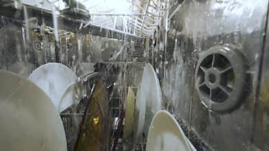 Slow-motion inside view of a running dishwasher with water splashing over plates and utensils, captured from a unique interior