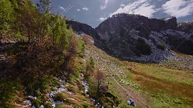 An aerial view from a FPV drone flies through a gorge along a river to a waterfall on a sunny summer day.