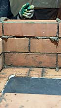 A stove fitter places a brick on clay mortar in a brickwork opening. Close-up. Construction of a heating stove. Vertical video