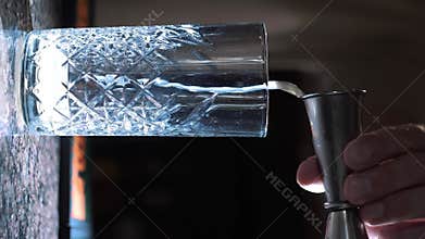 Bartender pouring alcoholic drink using beaker into glass with one hand.